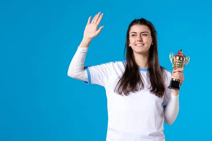 Smiling young woman waving and holding a gold trophy