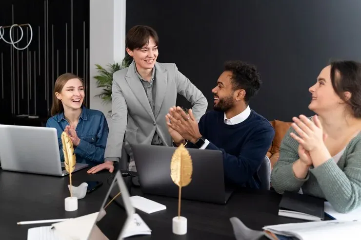 Smiling team applauding around a meeting table with laptops