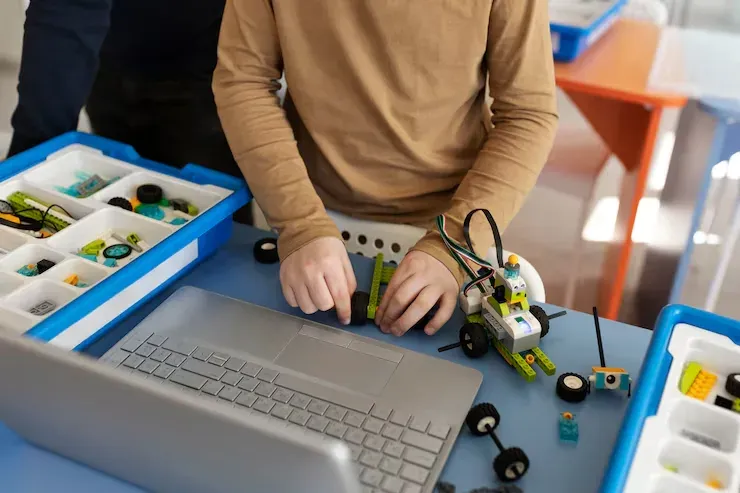 Student building a LEGO robot car next to a laptop