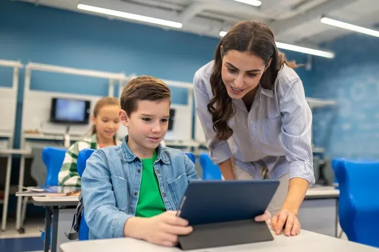 Teacher helping a boy use a tablet in a classroom