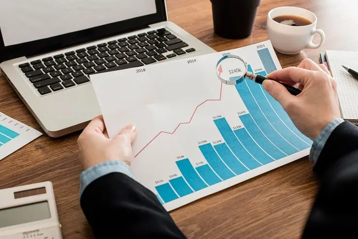 Hands holding a magnifying glass over a printed bar chart showing growth